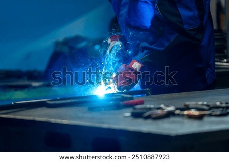 Welder using a torch, bright blue flame and sparks in a workshop, creating a strong weld on metal.