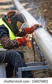Welder wearing protective clothing for welding industrial construction oil and gas or water and sewerage plumbing pipeline outside on site