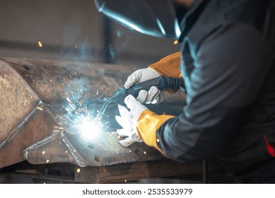 Welder wearing protective gear is joining metal parts in a factory, creating bright sparks - Powered by Shutterstock