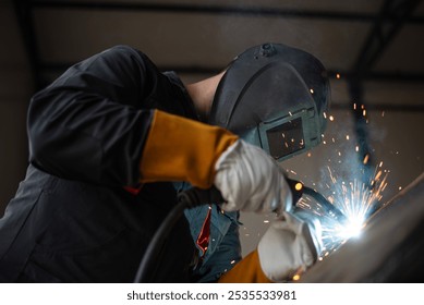 Welder wearing protective gear is joining metal parts together, creating a shower of sparks - Powered by Shutterstock