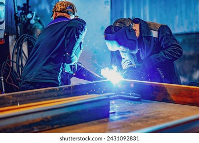 A welder wearing a protective mask for metal welding and protective gloves performs welding work at a metal structures plant. Welding a steel industrial beam. Sparks, hot flame from welding. - Powered by Shutterstock