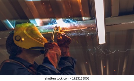 A welder wearing a yellow mask performs the work with a MIG-MAG welding machine. Production of welding works