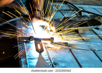 Welder Is Welding Metal Hook Melting Or Fusing The Two Parts Together By The Heat. Weldment Of A Steel Door. Long Exposure Of Welding Fires Flares From The Industrial Welding Factory