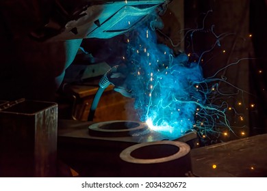 Welder is welding metal part in factory. Welder bonding metal with welding device in workshop, lots of sparks to be seen, he wears welding googles.