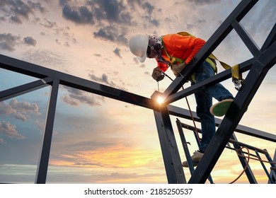 A welder is welding steel on a steel roof truss. Working at height equipment. Fall arrestor device for worker with hooks for safety body harness. Worker in construction site.