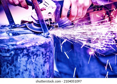 A welder welds metal into his workshop. Blue welding sparks. Gas combustion and blue smoke. Small welding workshop. Welding juncture of metal construction - Shutterstock ID 2104051097