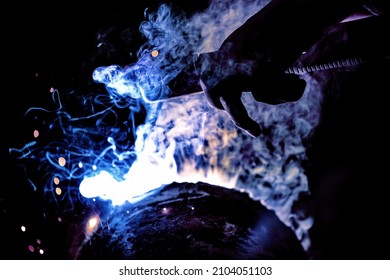 A welder welds metal into his workshop. Blue welding sparks. Gas combustion and blue smoke. Small welding workshop. Welding juncture of metal construction - Shutterstock ID 2104051103