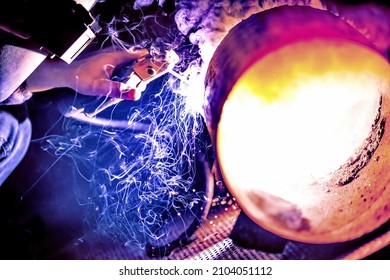 A welder welds metal into his workshop. Blue welding sparks. Gas combustion and blue smoke. Small welding workshop. Welding juncture of metal construction - Shutterstock ID 2104051112