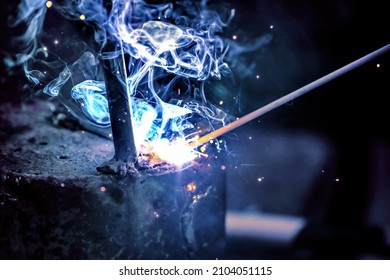 A welder welds metal into his workshop. Blue welding sparks. Gas combustion and blue smoke. Small welding workshop. Welding juncture of metal construction - Shutterstock ID 2104051115