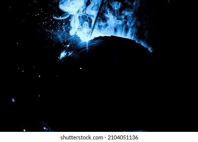 A welder welds metal into his workshop. Blue welding sparks. Gas combustion and blue smoke. Small welding workshop. Welding juncture of metal construction - Shutterstock ID 2104051136