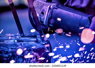 A welder welds metal into his workshop. Blue welding sparks. Gas combustion and blue smoke. Small welding workshop. Welding juncture of metal construction - Shutterstock ID 2104051139