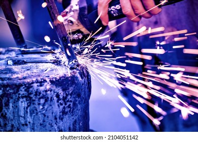 A welder welds metal into his workshop. Blue welding sparks. Gas combustion and blue smoke. Small welding workshop. Welding juncture of metal construction - Shutterstock ID 2104051142