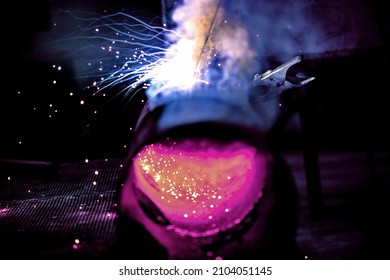 A welder welds metal into his workshop. Blue welding sparks. Gas combustion and blue smoke. Small welding workshop. Welding juncture of metal construction - Shutterstock ID 2104051145