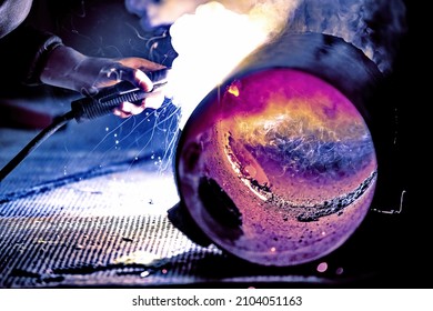 A welder welds metal into his workshop. Blue welding sparks. Gas combustion and blue smoke. Small welding workshop. Welding juncture of metal construction - Shutterstock ID 2104051163
