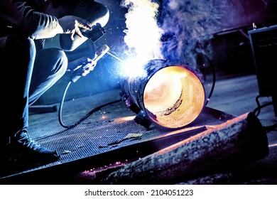 A welder welds metal into his workshop. Blue welding sparks. Gas combustion and blue smoke. Small welding workshop. Welding juncture of metal construction - Shutterstock ID 2104051223