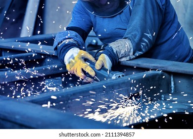 A welder welds metal into his workshop. Blue welding sparks. Gas combustion and blue smoke. Small welding workshop. Welding juncture of metal construction - Shutterstock ID 2111394857