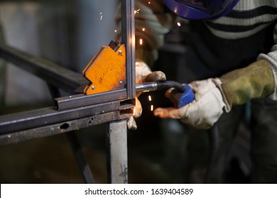 Welder At Work. The Welder Heats The Metal. Classes In The Workshop. Steel Processing. Welder In A Blue Welding Mask. High Melting Point Of Metal. A Man Doing Hard Work.