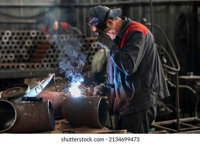 Welder at work. Man in protective glasses. The welder makes a seam between metal pipes. Sparks and smoke from welding.