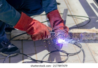 Welder At Work. The Welder's Hands Are Wearing Protective Gloves, Making Seams On Metal. Sparks And Smoke During Welding