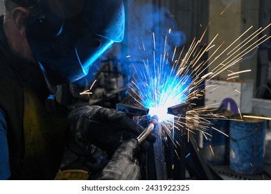 Welder at work. Welding sparkles. Male worker wearing helmet and gloves. Welding metal in factory. Close up of industrial worker at construction site. Man is working.  - Powered by Shutterstock