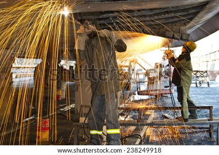 Welders on black metal, repairing a ship in dry dock