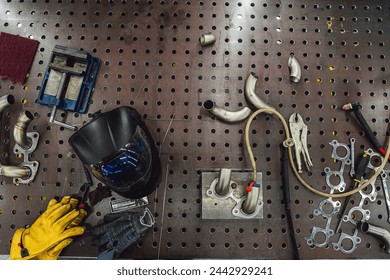 Welder's workplace. Welding equipment on an iron table with a welding helmet, leather gloves, a welding torch and the products to be welded. - Powered by Shutterstock