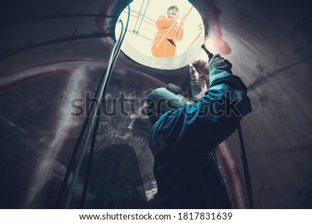 Welding arc argon worker male repaired metal is welding sparks industrial construction tank part manhole stainless oil inside confined spaces there is a watchman outside.
