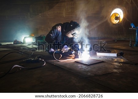 Welding male worker metal is part in machinery tank plate bottom construction petroleum oil and gas storage tank inside confined spaces.