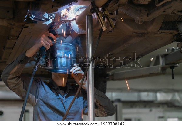 Welding\
metal products. Masked welder makes car\
repair