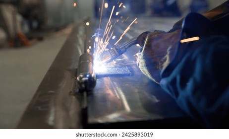 Welding with sparks close-up. Workers in industrial uniform and welded iron mask. Close-up of a welder welding metal. A welder in a mask welds metal and sparks the metal. - Powered by Shutterstock