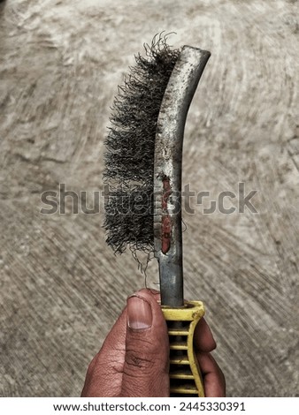 a welding wire brush that has been used for a long time and the wire is starting to become irregular, with a cement floor in the background