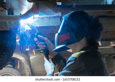 Welding work on a car, close-up. Mechanic in a welding mask welds the bottom of the car, selective focus - Shutterstock ID 1653708151