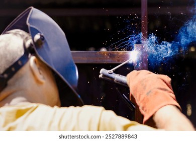 Welding Works. Welder Men Welds Metal Frame with Welding Rods on Dark Background. Welding Sparks and Smoke. - Powered by Shutterstock