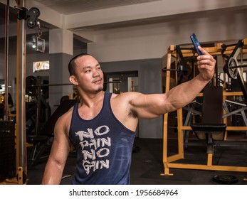 A Well Built And Rugged Man Takes A Selfie Of Himself For Social Media. A Modern Fitness Influencer Wearing A No Pain No Gain Tank Top.