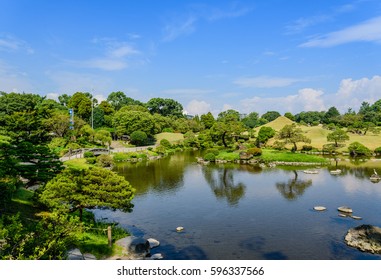 A well decorated Japanese garden with grass, trees and pond.The weather is fair and sunny.Clear water reflects the blue sky..