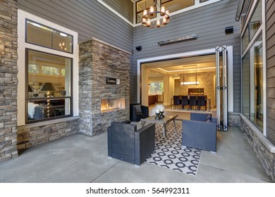 Well Designed Covered Patio Boasts Stone Fireplace, Wicker Patio Chairs Facing Gorgeous Rustic Wood Coffee Table Atop White And Black Geometric Rug. Northwest, USA
