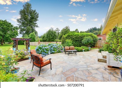 Well designed patio area with stone floor in the backyard of a yellow house. Relaxing area with comfortable outdoor furniture and blooming hydrangea flowers. Northwest, USA