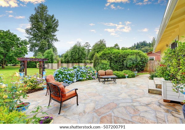 Well designed\
patio area with stone floor in the backyard of a yellow house.\
Relaxing area with comfortable outdoor furniture and blooming\
hydrangea flowers. Northwest,\
USA
