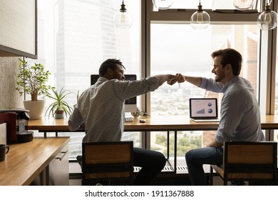 Well done, buddy. Motivated diverse young men coworkers bump fists on workplace feel excited achieve common goal. Two workers international business team members share success glad to help one another - Shutterstock ID 1911367888