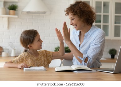 Well done dear. Excited mother give high five to small daughter praise child for reaching success in homework. Joyful female tutor greet schoolgirl for giving correct answer solving hard math problem
