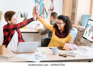 Well Done. Good-looking Inspired Young Smart Women Smiling And Giving A High-five While Working In The Office