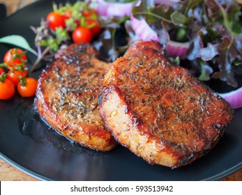 Well Done Grilled Pork Chop Steak In Black Plate And Vegetable Salad On Side