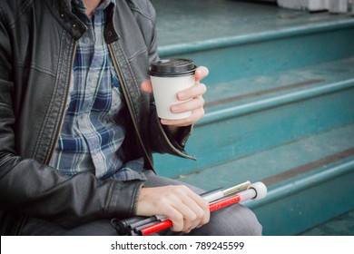 Well Dressed Blind Man Relaxing and Sitting on Steps Drinking a Coffee; Long White Cane Folded Up in Lap (Copy Space)