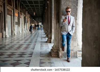 Well dressed European man using his mobile phone leaning against a column of the classic Italian colonnade architecture in Venice Italy