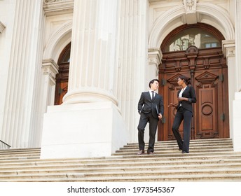 A well dressed man and woman in discussion as they as they walk down steps of a courthouse  building. Could be business or legal professionals. - Shutterstock ID 1973545367