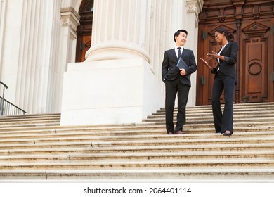 A well dressed man and woman smiling as they as they walk down steps of a courthouse  building. Could be business or legal professionals. - Shutterstock ID 2064401114