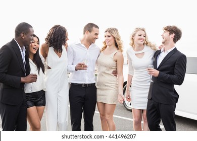 Well dressed people posing next to a limousine on a night out