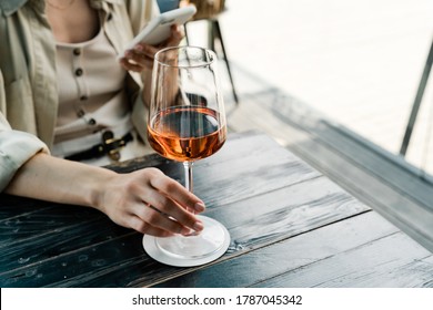 Well dressed woman holding glass with rose wine and using mobile phone