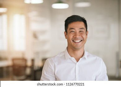 Well Dressed Young Asian Businessman Smiling While Standing By Himself In A Bright Modern Office