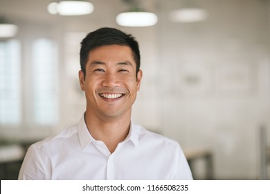 Well dressed young Asian businessman smiling confidently while standing alone in a bright modern office
